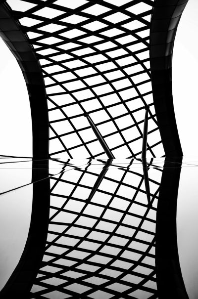 Black and white photograph of an abstract geometric grid pattern, forming the silhouette of curved architecture. The composition captures the architectural essence through symmetrical framing, with the focus on intricate details in monochrome tones. This artistic interpretation is set against a stark background to emphasize its unique structure, rendered in the style of an abstract geometric grid pattern. --ar 21:32