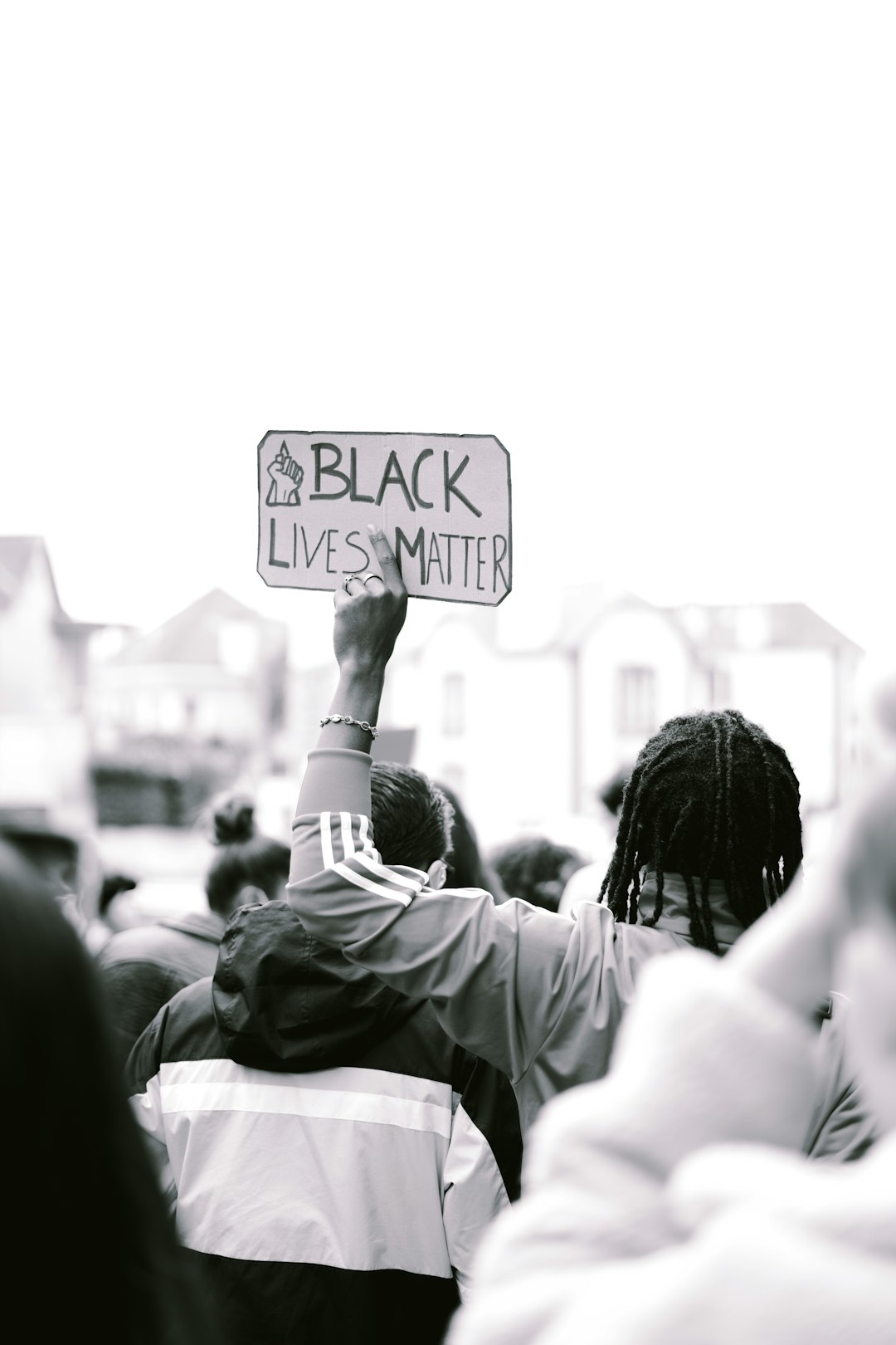 A person holding up an “BLACK LIVES MATTER” sign at the Black lives matter protest, with white and black colors, in the style of Leica M6 photography, shot from behind in a crowd of people, with high resolution and a grainy film filter, in a hyper realistic style. –ar 85:128