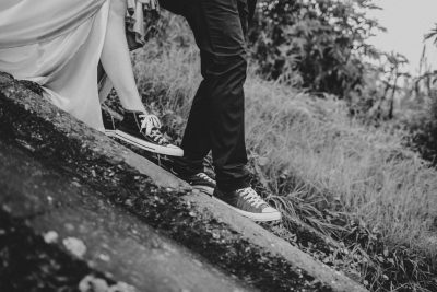 A black and white photo of the groom wearing converse, the bride in high heels standing on top of a cliff in an Indonesian mountain, wedding photography, taken with a Sony A7R IV camera, in the style of wedding photography. --ar 128:85