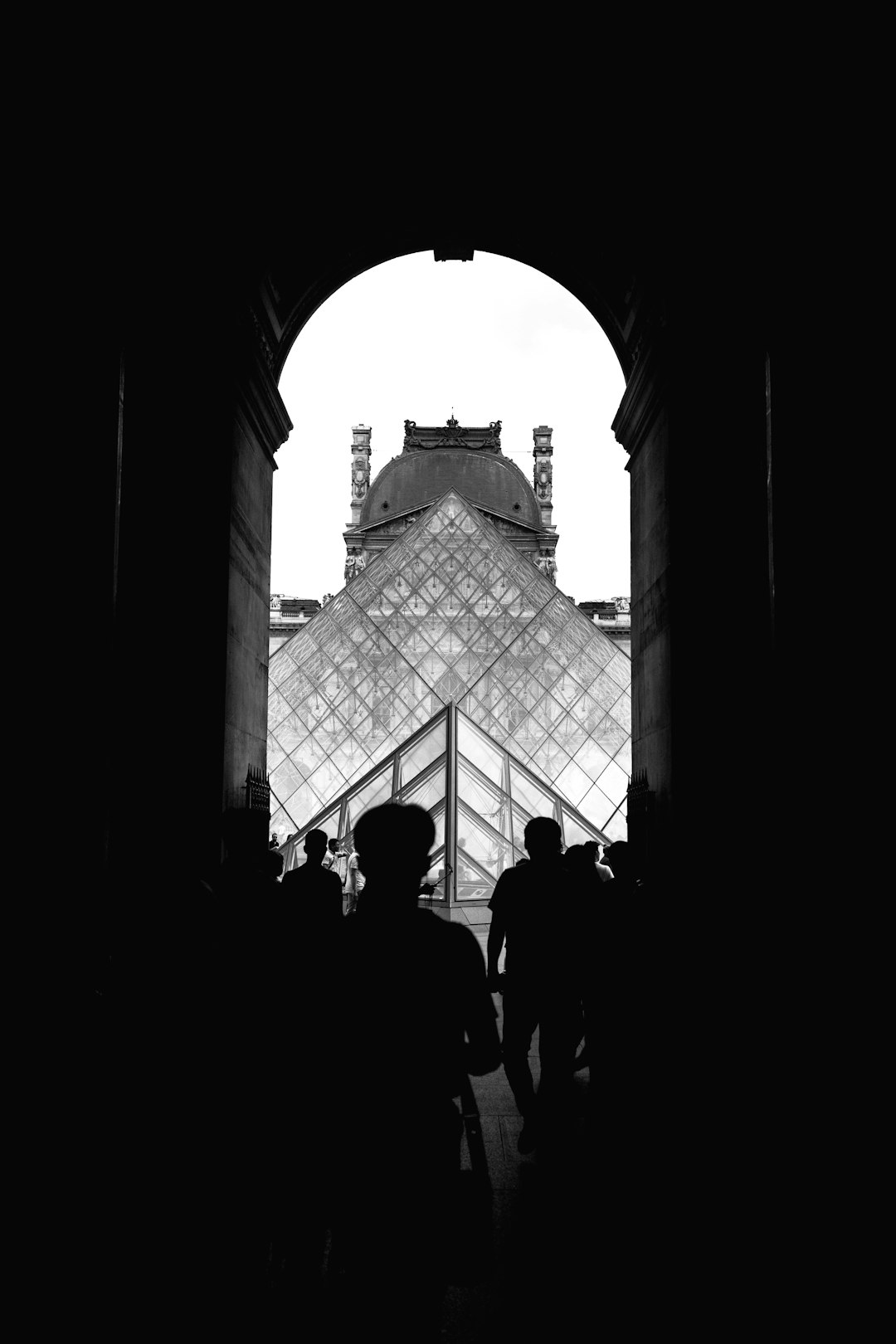 Black and white photo of the Louvre pyramid, seen from inside in silhouette with people walking around it, in the style of unsplash photography. –ar 85:128