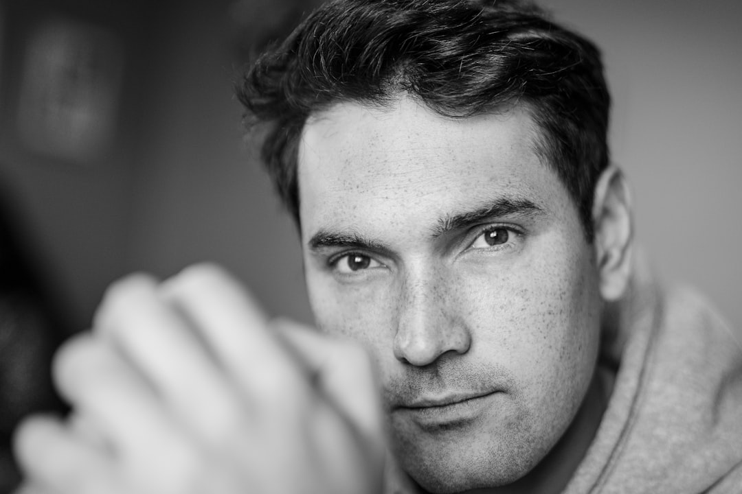 Black and white photo portrait of a man in his thirties, looking at the camera with an intense look on his face, hand reaching for the lens, wearing a sweatshirt, shot in the style of canon eos r5. –ar 128:85