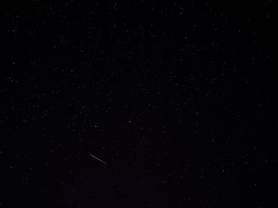 A dark night sky with stars, featuring one single shooting star in the upper left corner. The background is black and clear of any other objects. There is no foreground or depth to the scene, just the vastness of space. This photo was taken in the style of an iPhone camera, giving it a raw style. It captures the simplicity yet beauty of the night sky. --ar 4:3