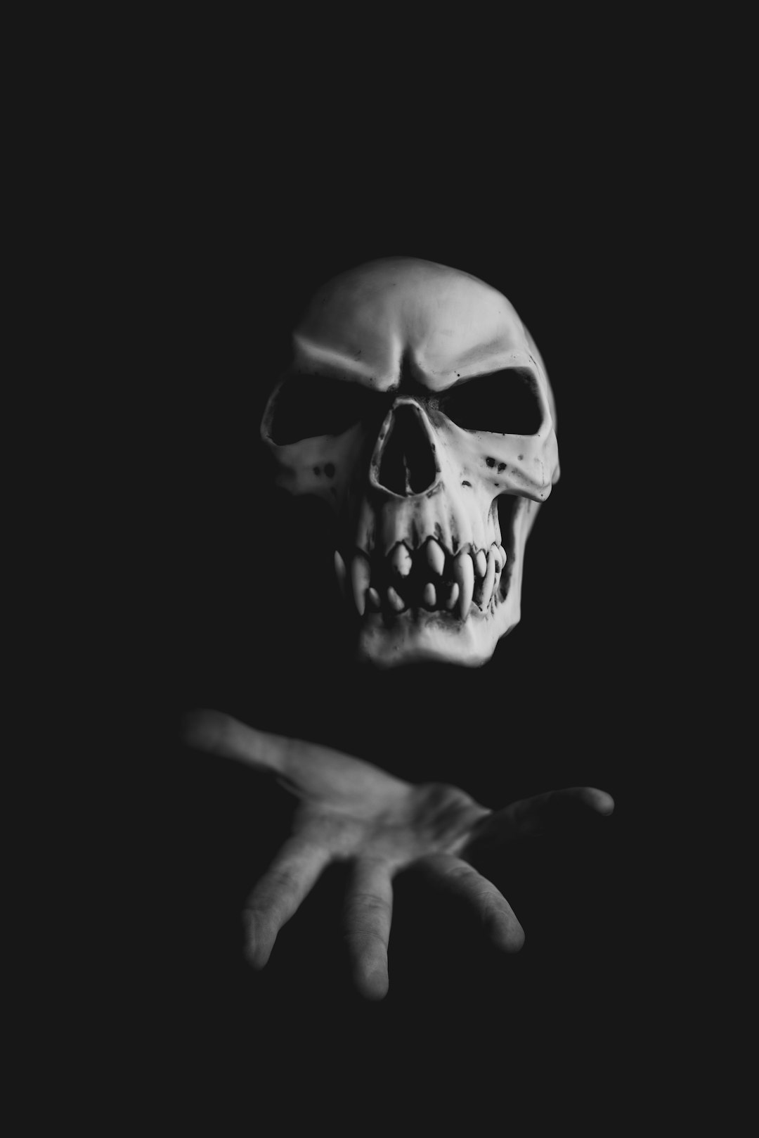 A skull with its hand outstretched on a dark background in black and white in the style of horror. –ar 85:128