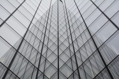 A glass building with diagonal patterned windows, creating an abstract and modern appearance. The building's tall walls feature symmetrical geometric shapes that create depth in the photograph. A person is seen climbing up one of these vertical panels, adding a human element to the architecture. --ar 128:85