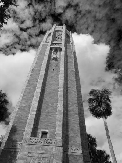 black and white photo of bok tower in florida, low angle shot, clouds, tower bell, palm trees --ar 95:128