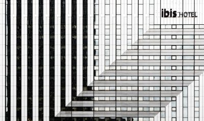 A black and white photograph of "ibis hotel" written on the side of an office building made from vertical lines in an architectural style. The pattern is symmetrical, with each line being one or two colors. This creates a minimalist design that emphasizes clean lines and geometric shapes. --ar 32:19