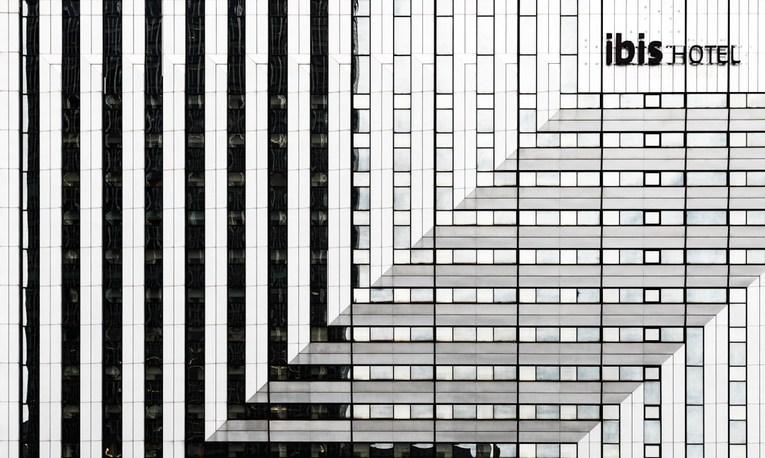 A black and white photograph of “ibis hotel” written on the side of an office building made from vertical lines in an architectural style. The pattern is symmetrical, with each line being one or two colors. This creates a minimalist design that emphasizes clean lines and geometric shapes. –ar 32:19