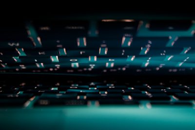 A closeup of the keyboard, illuminated from above and behind, with a blurred background, creating an atmosphere full of technology. The keys glow softly in shades of bluegreen against a dark backdrop. A shallow depth of field is used to focus on the glowing buttons while blurring out the surrounding environment. This composition creates a sense of mystery and futuristic ambiance. --ar 128:85