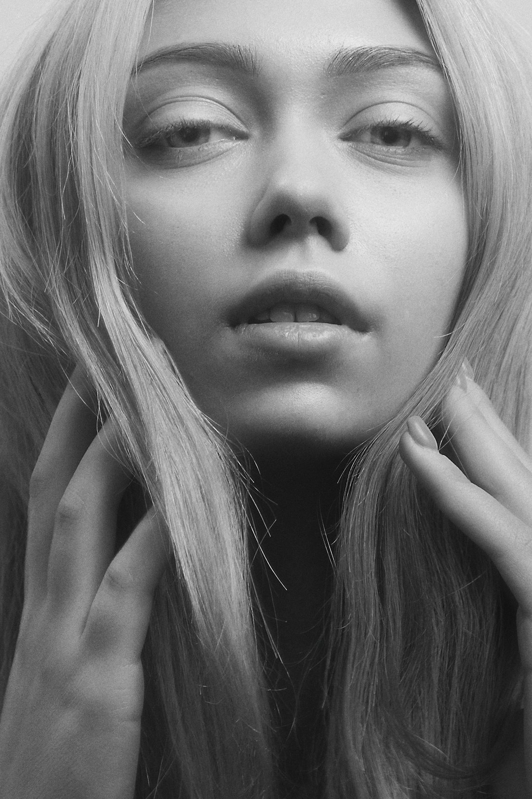 black and white photo of a beautiful woman with long blonde hair, hands on her face, soft lighting, facing the camera, looking straight at the viewer, shot in the style of [Petra Collins](https://goo.gl/search?artist%20Petra%20Collins) –ar 85:128