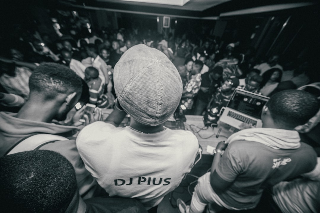 A crowd of people wearing white t-shirts with “DJplus” written on the back, standing in front of a DJ playing music at an African night club party. Black and white photography. The crowd watches the DJ playing music in the style of DJplus. –ar 128:85