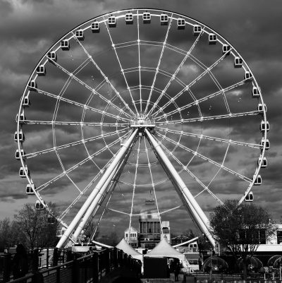 Black and white photo of the Ferris wheel at the harbor in Harrender, black sky, cloudy day, city background, large, round Ferris wheel, wide frame, high resolution, no people or cars around, high contrast, sharp details, HDR effect, perfect composition. --ar 127:128