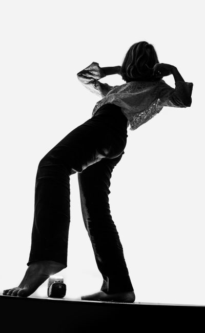 silhouette of woman in black pants and shirt, doing handstand on high heels against a white background, black and white photography with soft tones, studio photography shot in the style of Hasselblad X2D camera with a wideangle lens --ar 39:64