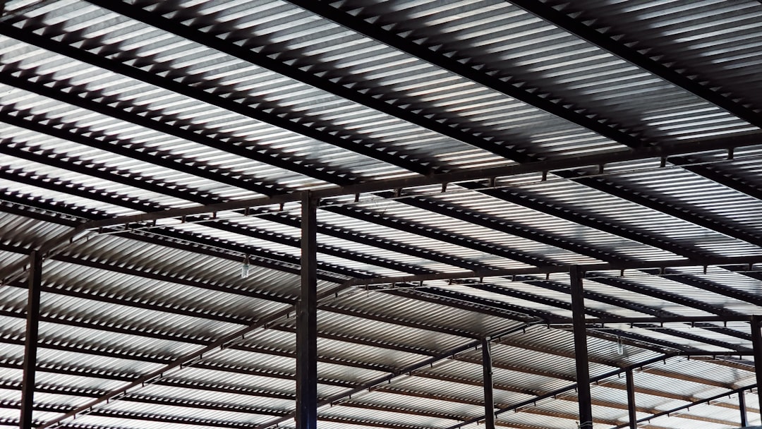 A steel roof structure with metal beams and rows of industrial building elements, which is an overhead view of the construction site. The light background creates a strong contrast between the white space and dark metallic structures. This photo captures the texture of high-quality material surfaces through macro photography in the style of industrial construction. –ar 16:9