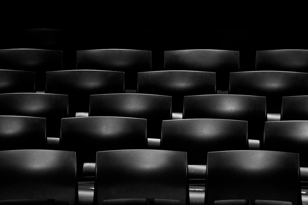 Black chairs in the cinema, black background, symmetrical composition, symmetrical lines, minimalism, high contrast, monochrome, soft light, high resolution photography, hyperrealistic details, depth of field, in the style of fujifilm xt4, f/28, 35mm –ar 128:85