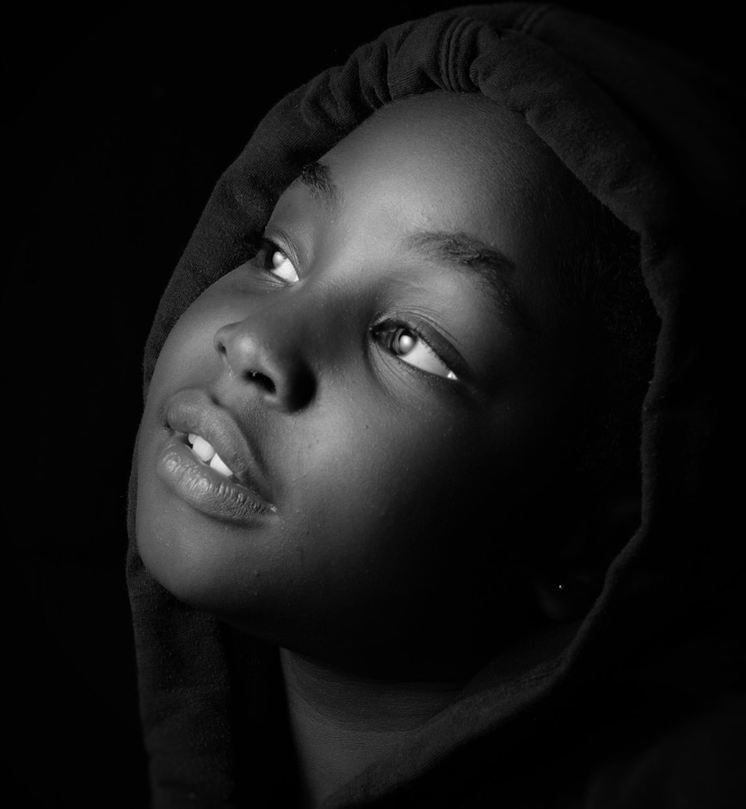 Black and white studio portrait of an African American teen girl wearing a hoodie, looking up with light in her eyes, high contrast, high resolution, high detail, taken with an 80mm lens at f/2.4, cinematic style with global illumination, in the style of no specific artist. –ar 59:64