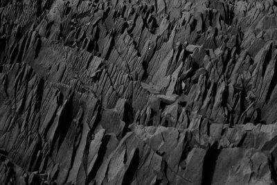 Black and white photograph of the rugged texture of black basalt rock, showcasing its unique patterns and textures in high contrast lighting. The focus is on capturing details that highlight shapes and features within the rocks, creating an atmosphere of natural beauty and mystery. --ar 128:85