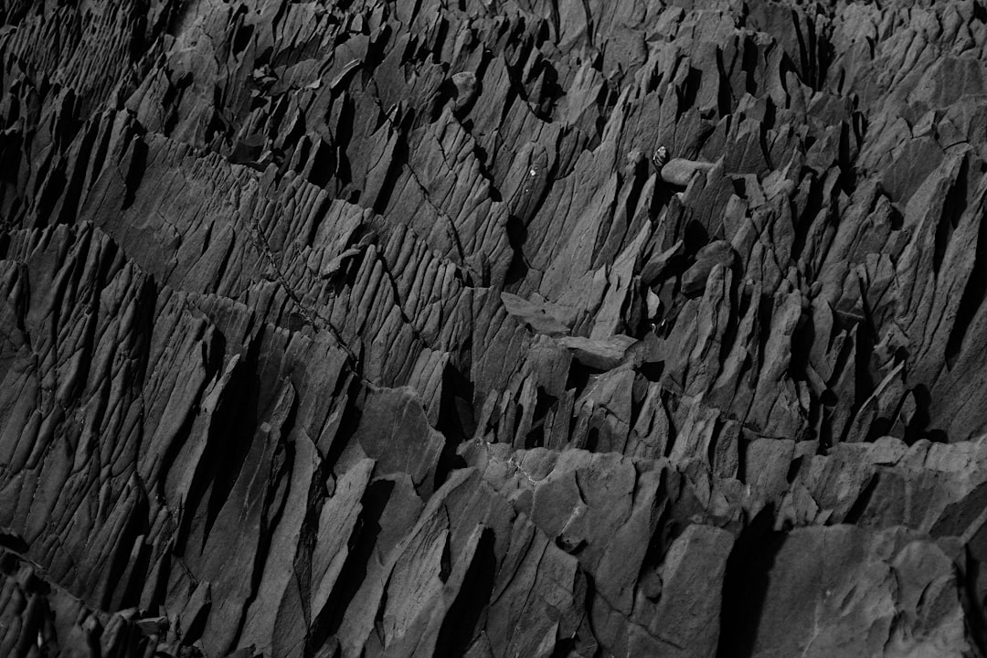 Black and white photograph of the rugged texture of black basalt rock, showcasing its unique patterns and textures in high contrast lighting. The focus is on capturing details that highlight shapes and features within the rocks, creating an atmosphere of natural beauty and mystery. –ar 128:85