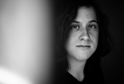 A portrait of an adult woman with freckles and shoulderlength hair, her face partially obscured by shadows in the room's low light. The photo is taken from close to eye level, focusing on capturing detailed expressions while maintaining a blackandwhite monochrome aesthetic. She has a neutral expression that reflects contemplation or introspection, standing against a dark background with soft lighting creating gentle highlights around his eyes. --ar 64:43