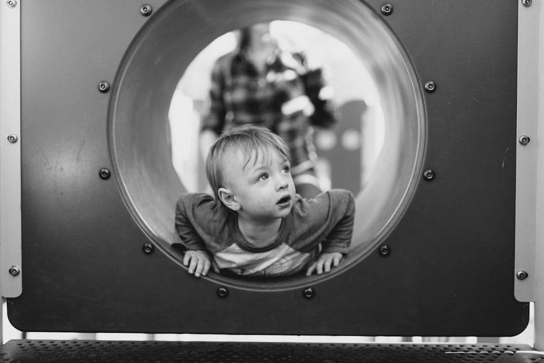 Black and white photography of one baby boy playing in the tunnel on the playground, with his parents watching from above. The view is through a round hole at the top center of the play structure, in the style of [Ansel Adams](https://goo.gl/search?artist%20Ansel%20Adams). –ar 128:85