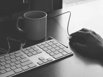 Black and white photo of a hand on a computer mouse, keyboard with a coffee mug nearby. The photo is in the style of an anonymous artist. --ar 4:3