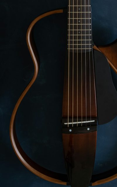 A closeup of the neck and body, showcasing its unique shape with visible wood grain patterns. The guitar's dark brown finish contrasts against a deep blue background, emphasizing the minimalist design. Shot from an overhead perspective to highlight the contours and curves on each side of the body. --ar 5:8