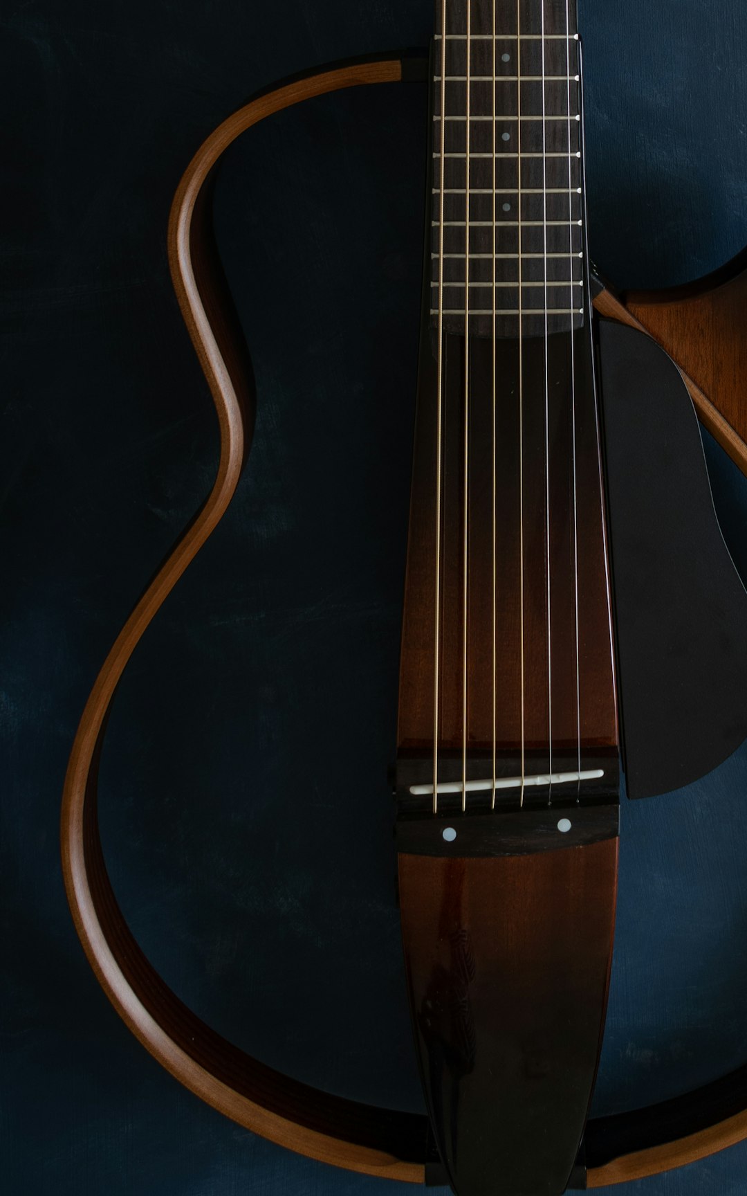 A closeup of the neck and body, showcasing its unique shape with visible wood grain patterns. The guitar’s dark brown finish contrasts against a deep blue background, emphasizing the minimalist design. Shot from an overhead perspective to highlight the contours and curves on each side of the body. –ar 5:8