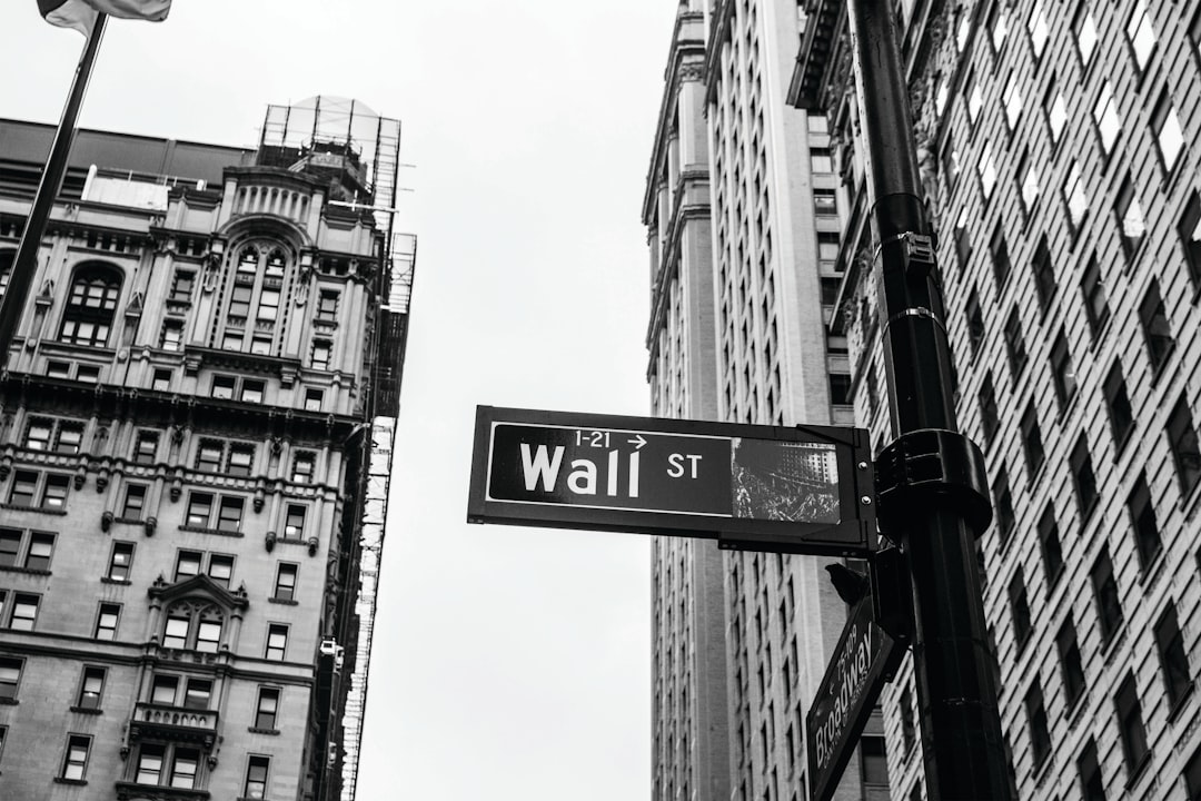 Wall Street sign, black and white photography, high resolution, Canon R5 camera, wide angle lens, iconic financial district buildings in the background, stock market trading graphic on street pole, focus on cityscape and clear sky. Black & White Photography in the style of Canon R5. –ar 128:85