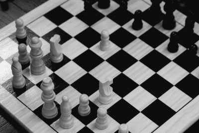 A chessboard with white and black pieces, viewed from above. The composition is symmetrically with the board's edges clearly defined in both colors. There is an empty space between two pawns on one side of opposite sides of the table. Captured using a Fujifilm XT4 camera with a f/2 lens. In the style of black and white. --ar 128:85