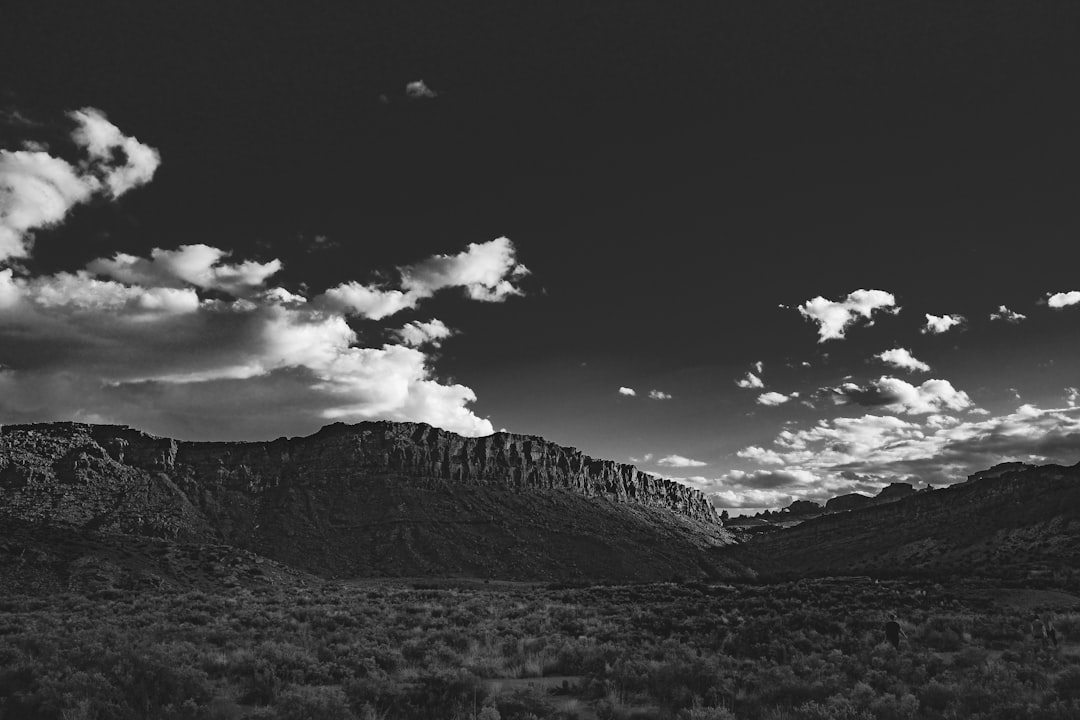 Black and white landscape photograph of the red rock mountains in St Louis, Utah. A few clouds scattered across the sky. Wide angle. Kodak TMax black & white film was used. A Sony Alpha A7 III camera with an aperture setting of f/8 was used to create sharp focus on details while softly blurring background elements. High contrast lighting gives the photograph a style reminiscent of [Ansel Adams](https://goo.gl/search?artist%20Ansel%20Adams). –ar 128:85