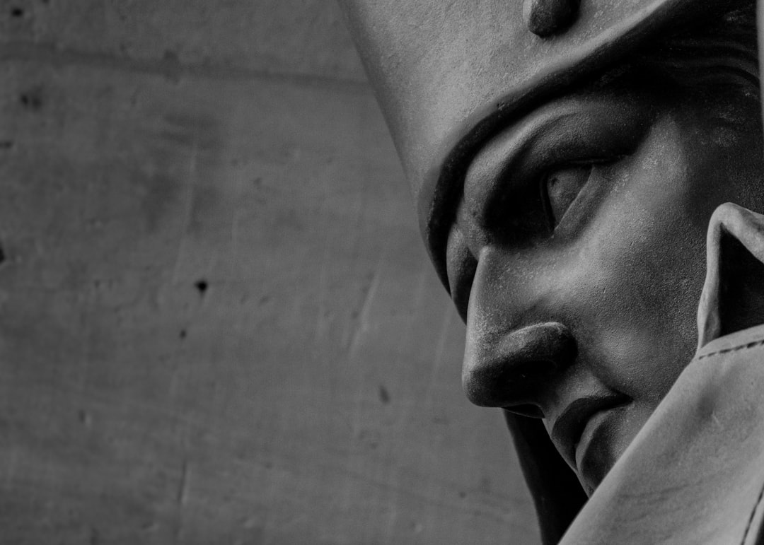 Black and white close up photo of an ancient Roman soldier wearing a mask and looking down at the ground. He is wearing a helmet with a flat top hat. The soldier’s face is not visible. It is a stone statue viewed from the side. The style is that of a documentary photograph. –ar 128:91