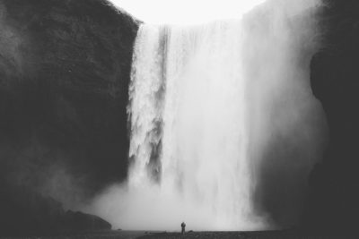 black and white photo of the waterfall in Iceland, a small person standing under it, foggy, low angle shot, unsplash photography style, in the style of unsplash --ar 128:85