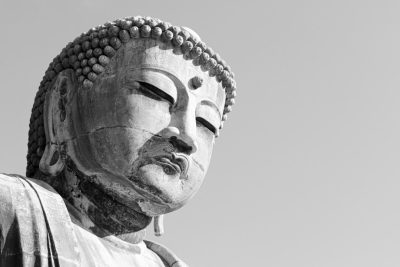 Black and white photography of the top half of an ancient Japanese Buddha statue, capturing its serene expression against a clear sky background. The focus is on the face of the buddha in high resolution. This photograph evokes a sense of tranquility through detailed attention to facial features, including eyes that convey peace and calmness in the style of a Japanese photographer. --ar 128:85