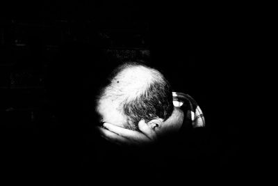 black and white photograph of an old man's hand holding his head, his hair is balding, in the shadows, dimly lit, black background, --ar 128:85