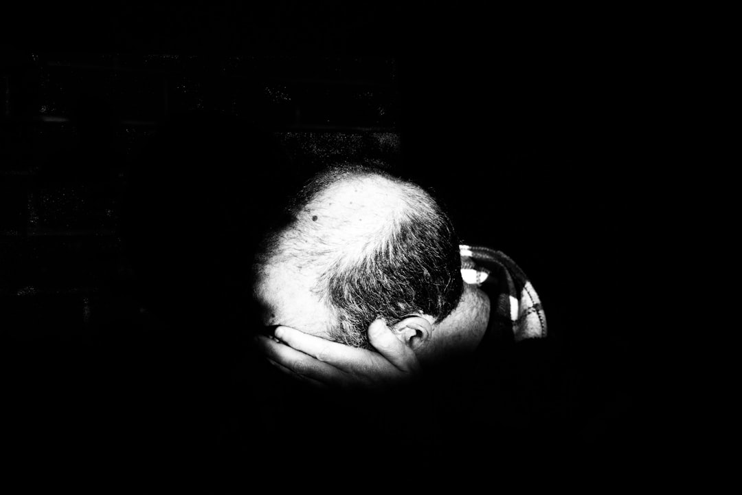 black and white photograph of an old man’s hand holding his head, his hair is balding, in the shadows, dimly lit, black background, –ar 128:85