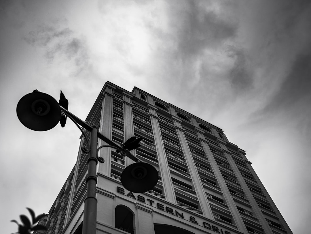 A black and white photo of the top floor corner exterior wall of a hotel with “EASTʻ.Sâtler & Driv” written on it, a large street light in front of the building, a cloudy sky, taken from a low angle, captured with a canon eos r5 camera. –ar 4:3