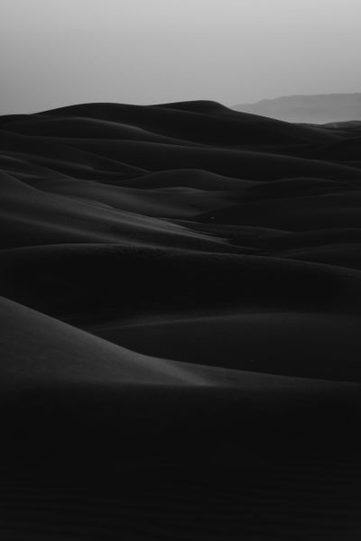 Black and white photo of the dunes in Saudi Arabia, minimalism, cinematic, moody, dark tones, low contrast, low saturation, beautiful, grainy. The photo has a minimalist style with cinematic and moody tones created with dark colors, low contrast and saturation. It depicts the dunes in Saudi Arabia in a beautiful and grainy black and white image. --ar 85:128