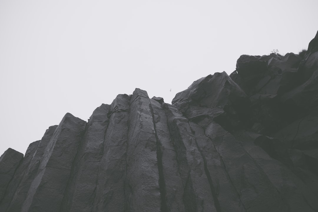 Low angle photo of a rock cliff against a gray sky with low contrast, minimalist and in the style of black and white film with a grainy filter, sharp focus and a hyper realistic style. –ar 128:85