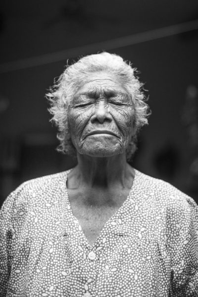 A black and white portrait of an elderly woman in the style of [Dorothea Lange](https://goo.gl/search?artist%20Dorothea%20Lange), wearing a patterned dress, standing straight with her eyes closed and looking at the camera, with a simple background, captured in the style of Leica M6 using Portra 800 film. --ar 85:128