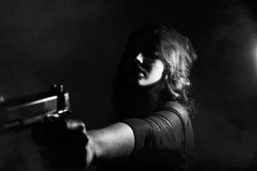 A woman with long hair is pointing her gun at the camera, her face illuminated in the style of light from behind. The background of the scene has dark tones and there’s no detail on it in black and white. –ar 128:85