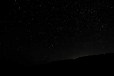 A black sky with stars, at night, a dark silhouette in the top left corner, distant mountains in the bottom right corner, high resolution, high quality, high detail, super realistic, cinematic, professional photography, shot with a canon r3 camera, depth of field, volumetric light, natural light, in the style of no artist. --ar 128:85