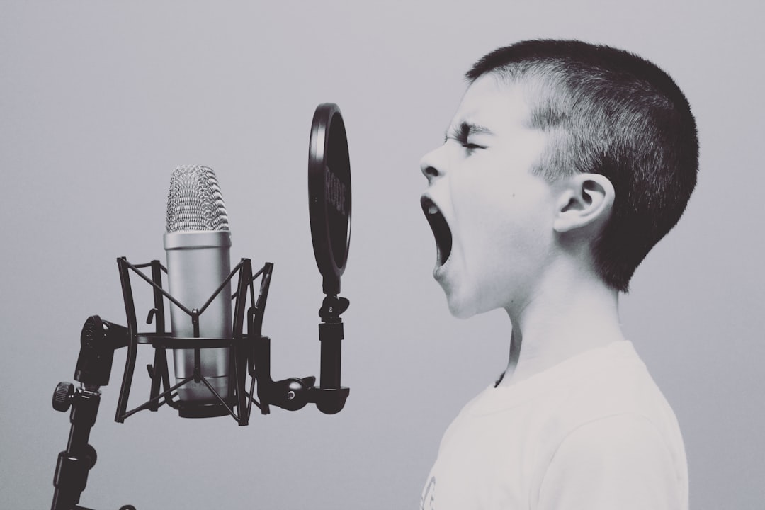 A boy with short hair is shouting into the microphone, which stands in front of and on top of him. The background color should be white. He wears light colored . In the style of black and white photography. –ar 128:85