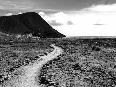 Black and white photography of the trail to SignUnde, Lanzarote in Spain, with black rocks, mountains, and ocean. The image is in the style of a minimalist landscape photograph. --ar 4:3