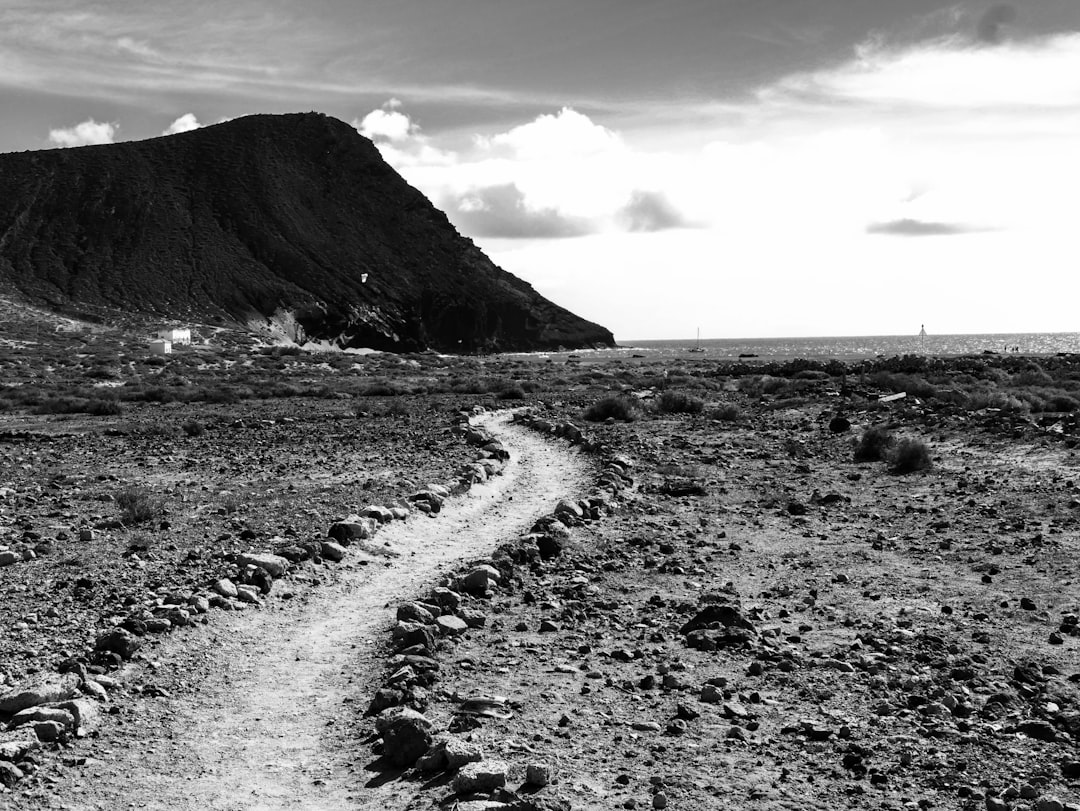 Black and white photography of the trail to SignUnde, Lanzarote in Spain, with black rocks, mountains, and ocean. The image is in the style of a minimalist landscape photograph. –ar 4:3