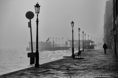 black and white photography, Venice, seafront with lanterns along the quay on a foggy morning, few people walking on the street, in the style of [Ansel Adams](https://goo.gl/search?artist%20Ansel%20Adams). --ar 128:85