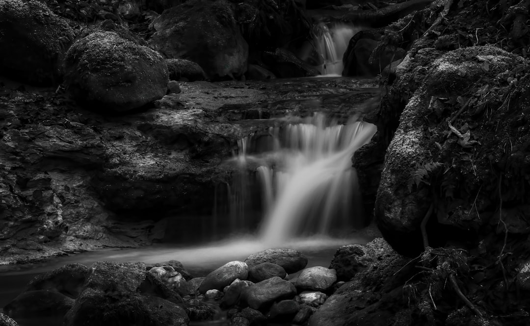 black and white long exposure photo of a small waterfall in the woods, rocks, dark, cinematic –ar 64:39