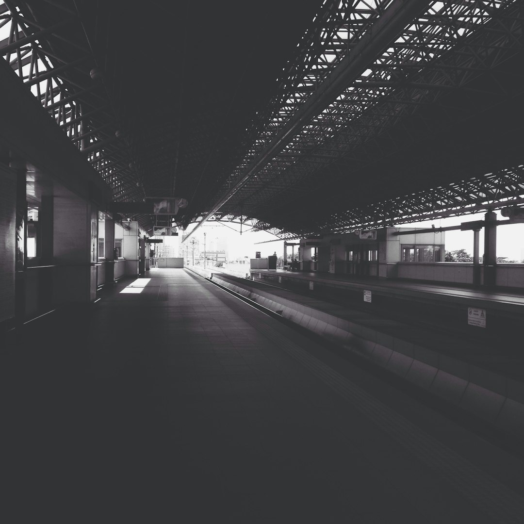 an empty train station platform, in the distance there is an open roofed over with steel beams, black and white photography, film grain, grainy, moody, atmospheric, hyper realistic