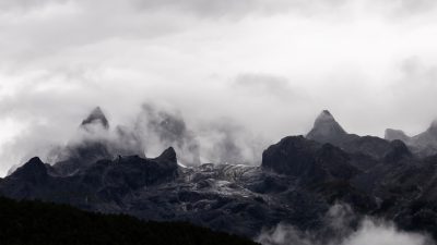 The rugged peaks of the Alps stand tall against an overcast sky, their silhouettes obscured by thick clouds and mist that swirl around them. The scene captures the raw beauty of nature's grandeur with its towering rock formations, dramatic mountain range, and dense fog creating a sense of mystery and awe in each frame. --ar 16:9