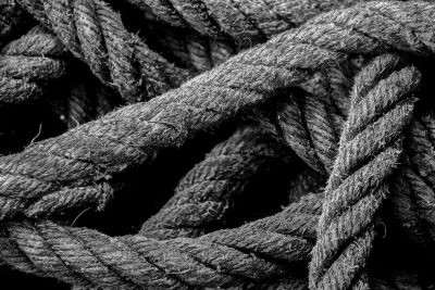Black and white photo of an old rope, detailed texture, closeup shot, high contrast between the black hues of ropes against dark background, natural lighting, Nikon D850 used for sharpness and depth of field. The photo was taken in the style of a documentary style. --ar 128:85