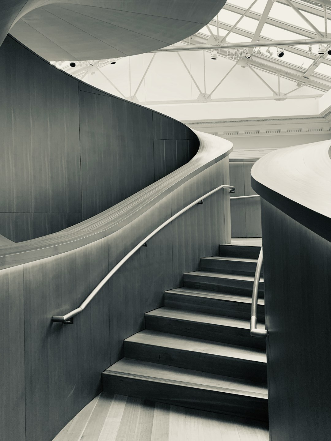 museum interior, staircase made of black oak wood and white metal handrail, curved shapes, grey walls, glass roof, photo taken in the style of Leica M6 camera in high resolution –ar 3:4