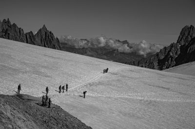 Black and white photography of people climbing the Montios in China sculpted in the style of nature, with snowcovered peaks and pristine alpine meadows. The scene captures their determination as they make their way on an icy path leading to freedom. The contrast between black & white creates a dramatic effect. --ar 128:85